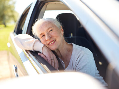 road trip, travel and old people concept - happy senior woman driving in car with open window