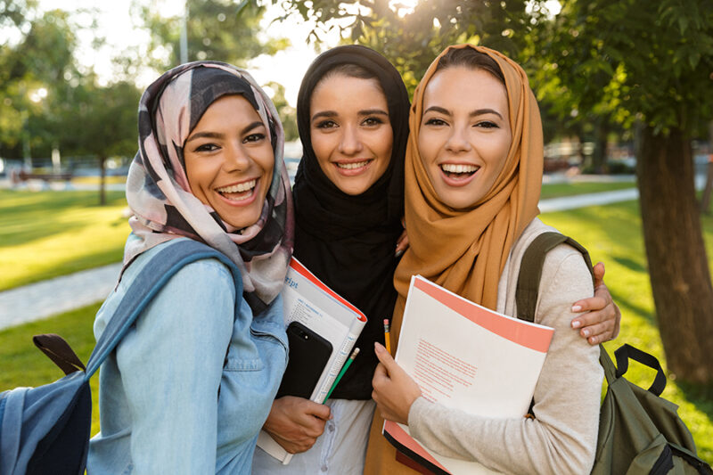 Image of a happy young arabian women students holding books in park outdoors.